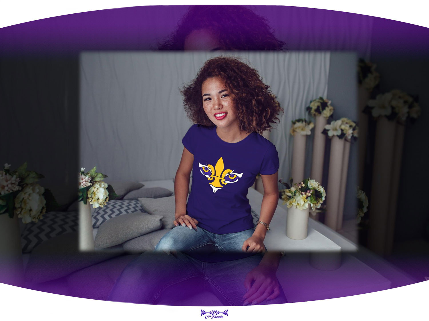 Woman sitting on bed smiling wearing purple LSU female fitted tee with a gold and white fleur de lis with tiger eyes on the chest